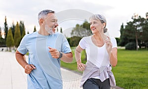 Happy senior husband and wife in sportive outfits running outdoors in city park