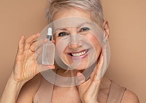 Happy senior lady applies cosmetic oil serum on face takes care of skin and smiles broadly enjoys beauty treatments
