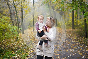 Happy senior lady and a little toddler girl, grandmother and granddaughter, enjoying a walk in autumn park