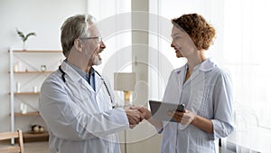 Happy senior male doctor physician handshaking young female nurse