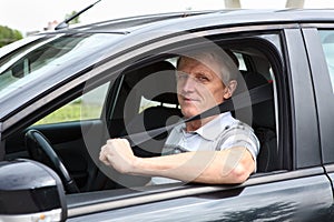 Happy senior male fastens safety belt sitting in car