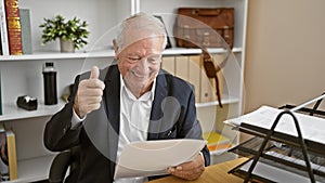 Happy senior man confidently doing thumb up gesture at the office while reading business document, proving his success at work as