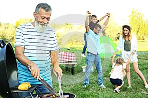Happy senior man cooking food on barbecue grill and his family