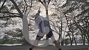 Happy senior man exercise and stretching at lake park under tree in evening sunset. asian elderly men outdoor activity workout. fi