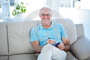 Happy senior man in eyeglasses sitting on sofa with clipboard