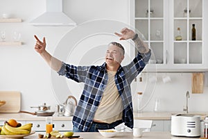 Happy senior man fooling around and dancing while cooking breakfast in kitchen interior, free space