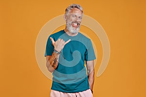 Happy senior man gesturing and smiling while standing against orange background