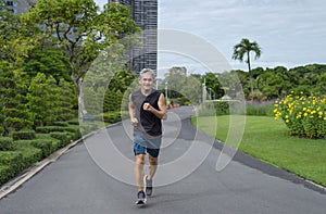 Happy senior man with grey hair in sportswear running  in the city park
