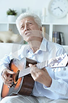 Happy senior man with guitar sitting on the sofa at home