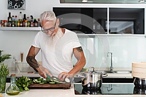 Happy senior man having fun cooking at home - Elderly person preparing health lunch in modern kitchen