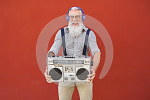 Happy senior man having fun listening to music with wireless headphones and vintage boombox outdoor