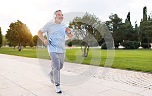 Happy senior man in headphones listening music while jogging outside in city park