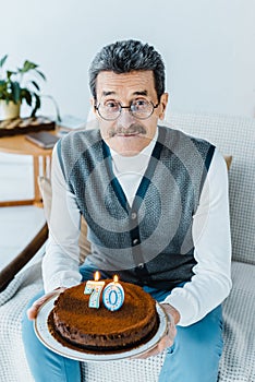 Happy senior man holding birthday cake while sitting on sofa a in