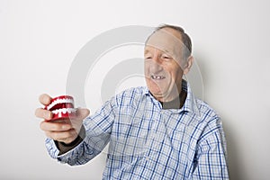 Happy senior man holding dentures against gray background photo