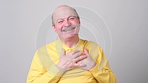 Happy senior man holding palm on heart and smiling thankful receiving compliment