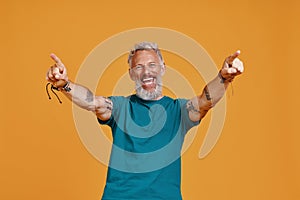 Happy senior man keeping arms outstretched and smiling while standing against orange background