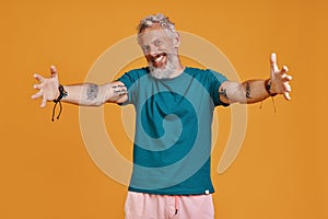Happy senior man keeping arms outstretched and smiling while standing against orange background