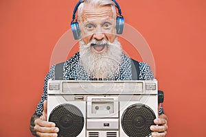 Happy senior man listening to music with boombox and headphones outdoor - Crazy hipster male having fun with vintage stereo