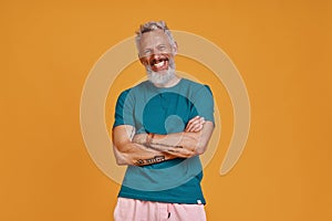 Happy senior man looking at camera and smiling while standing against orange background