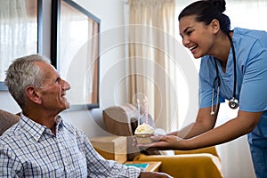 Happy senior man looking at doctor holding cup cake with candle in nursing home