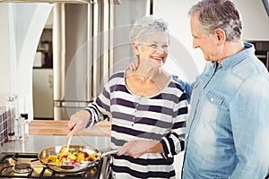 Happy senior man looking at wife cooking food