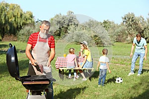 Happy senior man with meat at barbecue grill and his family having picnic