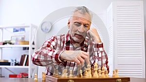 Happy senior man playing chess alone, training for chess competition, checkmate