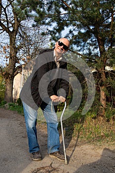 Happy senior man posing with a walking stick in sunny day