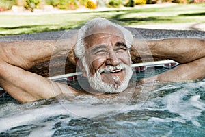 Happy senior man relaxing at the edge of swimming pool