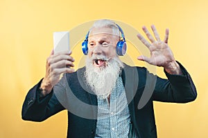 Happy senior man taking selfie while listening music with headphones - Hipster beard male having fun using mobile smartphone