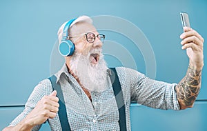 Happy senior man taking selfie while listening music with headphones - Hipster mature male having fun using mobile smartphone