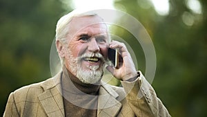 Happy senior man talking on phone in park, mobile communication, technology
