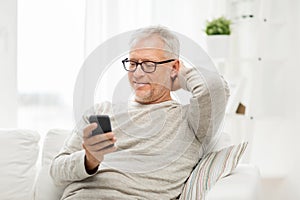 Happy senior man texting on smartphone at home