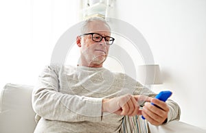 Happy senior man texting on smartphone at home