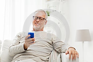 Happy senior man texting on smartphone at home