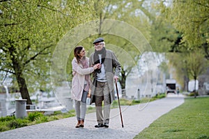 Happy senior man with walking stick and adult daughter outdoors on a walk in park.