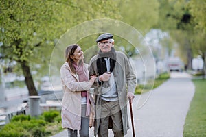 Happy senior man with walking stick and adult daughter outdoors on a walk in park.