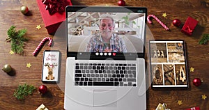 Happy senior man waving on video call on laptop, with smartphone, tablet and decorations