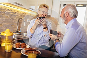 Senior man and woman couple sitting together at home smiling and drinking tea or coffee