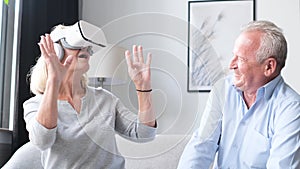 Happy senior man and woman wearing virtual reality headset at home sitting on sofa.