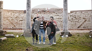 Happy senior man and women with young girl waving on video chat with family near old amphitheater ruins in Ostia, Italy.