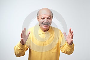 Happy senior man in yellow tshirt celebrating his success over gray background