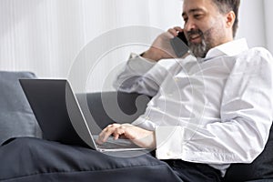Happy senior manager business man relax at office sofa calling with friend while using laptop comfortable success people lifestyle