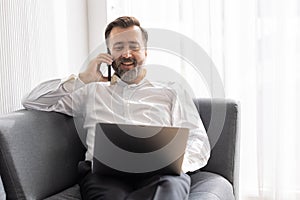 Happy senior manager business man relax at office sofa calling with friend while using laptop comfortable success people lifestyle