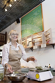 Happy senior merchant measuring ingredient on weight scale in spice store