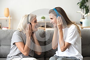 Happy senior mother and adult daughter listening music in headph