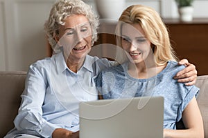 Happy senior mother and adult daughter using laptop