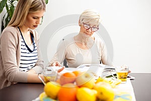 Happy senior mother and her daughter looking at family photo album while sitting at a dining table.