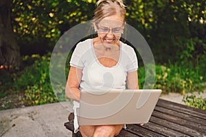 Happy senior old woman working online with laptop computer outdoor in garden