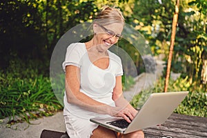 Happy senior old woman working online with laptop computer outdoor in garden